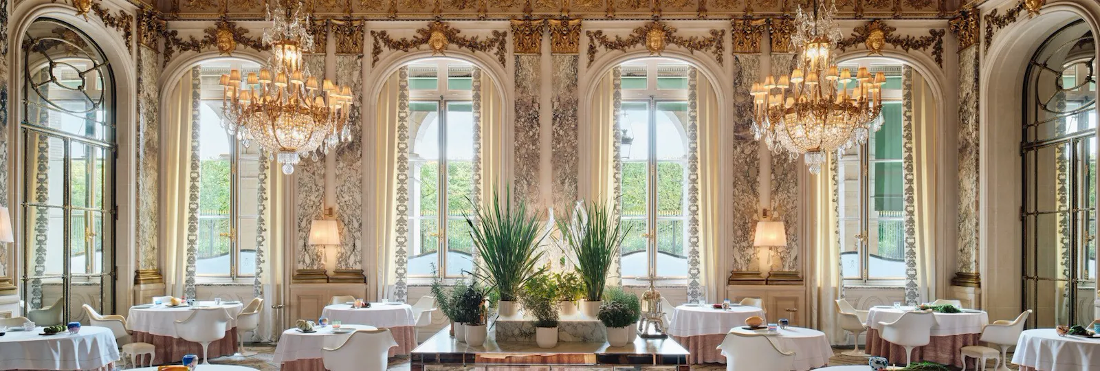 Grande vue du restaurant le Meurice Alain Ducasse avec des chaises et des tables autour d’un mobilier avec des plantes et un verre de Murano sur le dessus, au Meurice, Paris