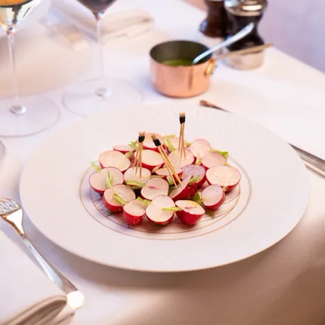 Plate of sliced radishes with toothpicks, wine glasses, and salt and pepper shakers on a white table.