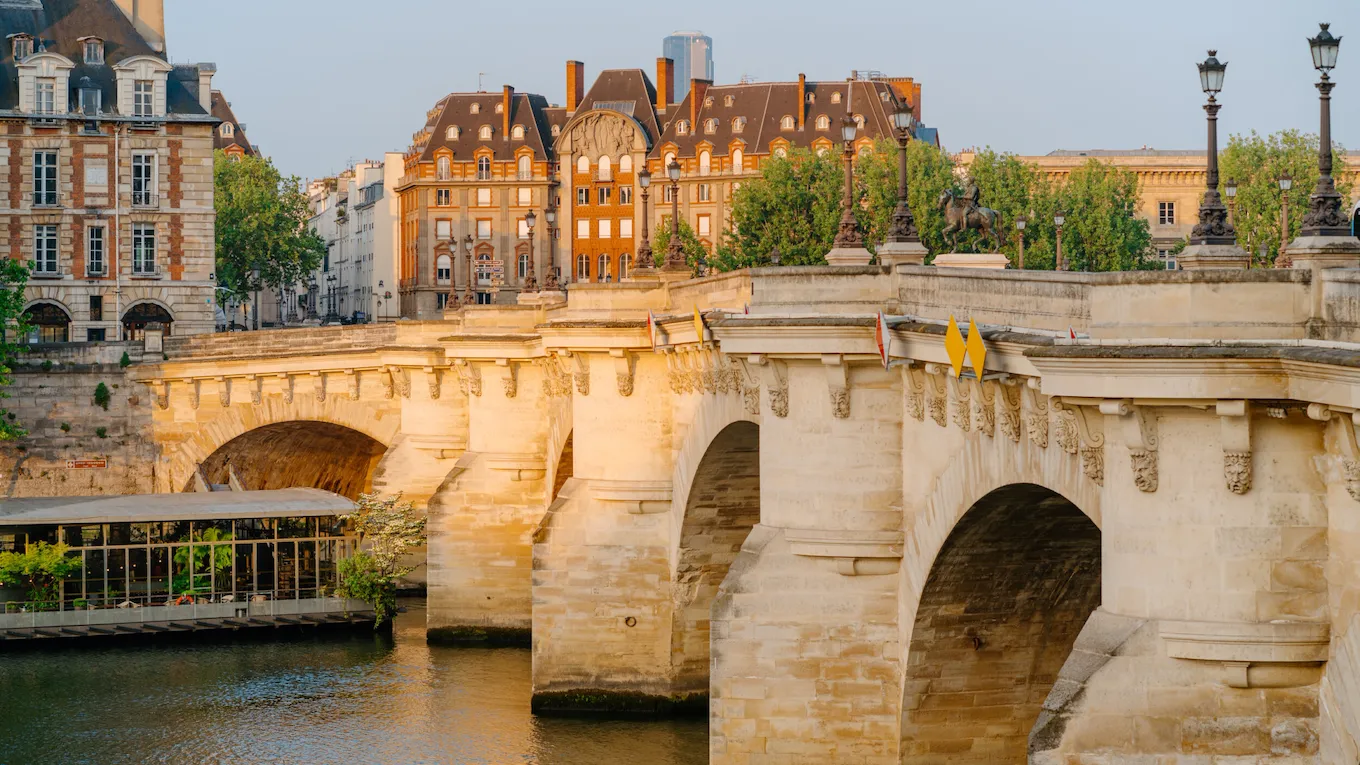 View of the Pont Neuf at sunrise, the Seine, and a boat filled with trees on the water, at Pont Neuf, Paris.