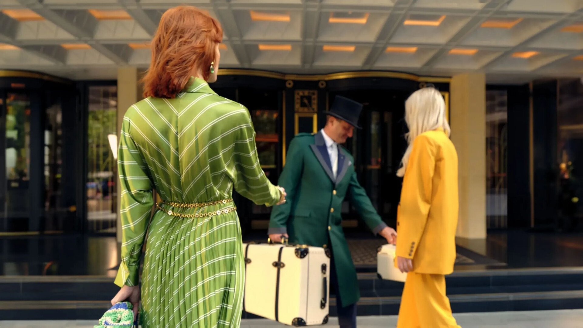 Image of a person in a green dress walking into the entrance of The Dorchester as Doorman in a green coat greets them and takes  their bag