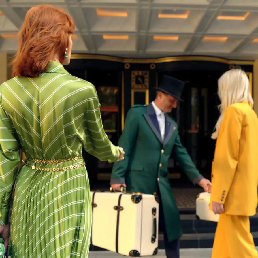 Image of a person in a green dress walking into the entrance of The Dorchester as Doorman in a green coat greets them and takes their bag