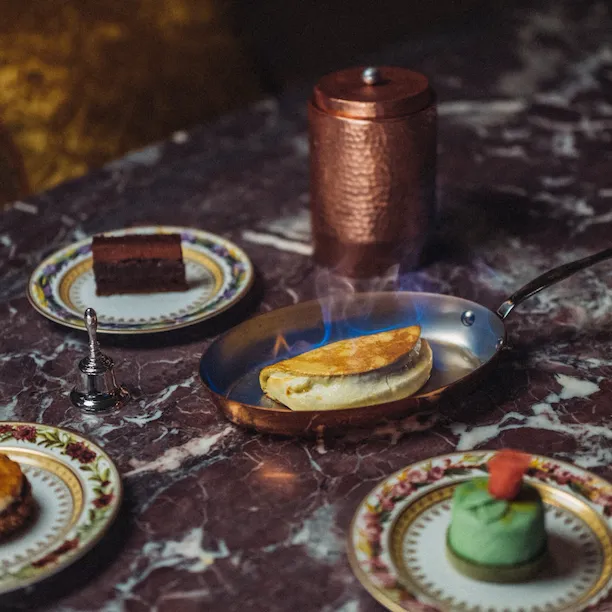 Assortiment de desserts sur une table en marbre avec une crêpe soufflée en feu, charlotte au chocolat et gâteau Ambassadeur, au Jean Imbert au Plaza Athénée, à l’Hôtel Plaza Athénée, Paris