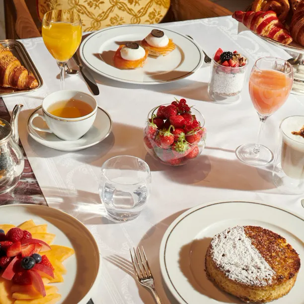 Images du brunch en salle Images du brunch au Jean Imbert au Plaza Athénée. On peut y voir une salade de fruits, des viennoiseries, du café, des oeufs et des jus de fruits.