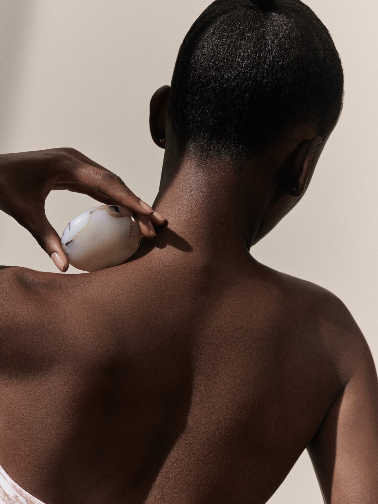 Dior Spa Plaza Athénée's iconography for spa treatments. Here, a dark-skin female model seen from the back and posing with a stone hold against the left-side of her neck.
