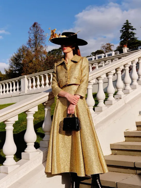 A person in a hat and gold skit standing on the stairs that lead from the croquet lawn to the rose garden in the Grounds of Coworth Park