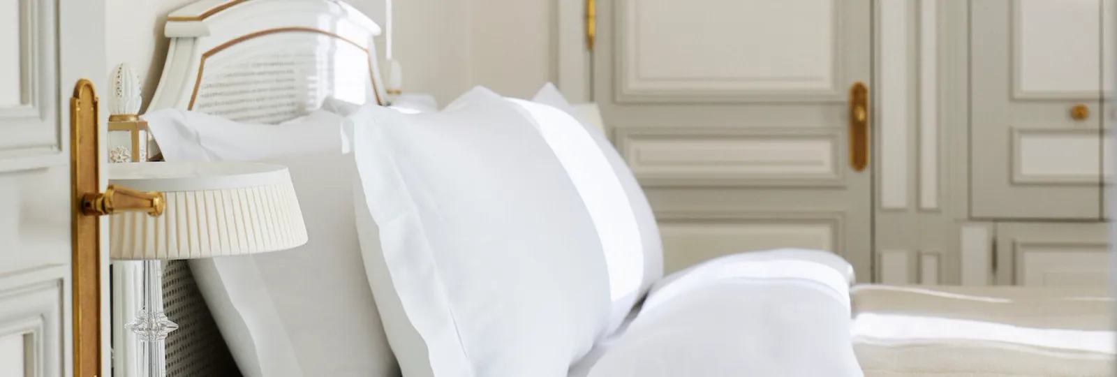 Bedroom in beige and white shades with a wooden closet in the background and a queen bed. At Le Meurice, Paris.