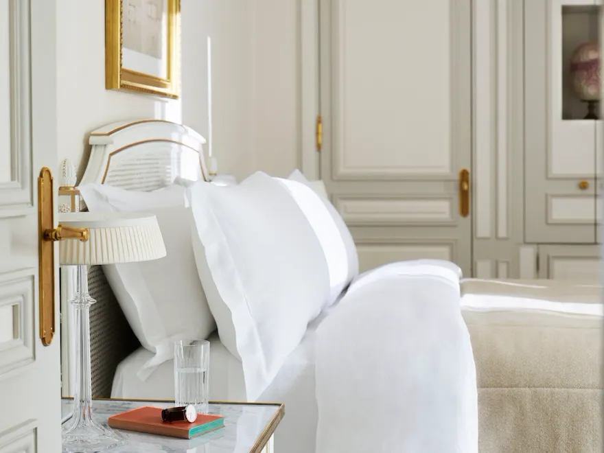 Bedroom in beige and white shades with a wooden closet in the background and a queen bed. At Le Meurice, Paris.