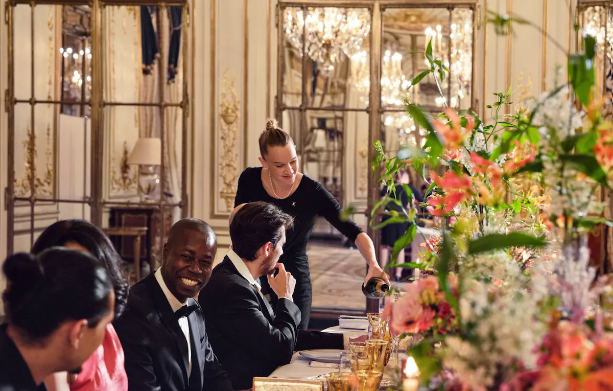 Women serving champagne to guests, sitting at the table, during a dinner in Le Salon Pompadour at Le Meurice, Paris - Dorchester Collection