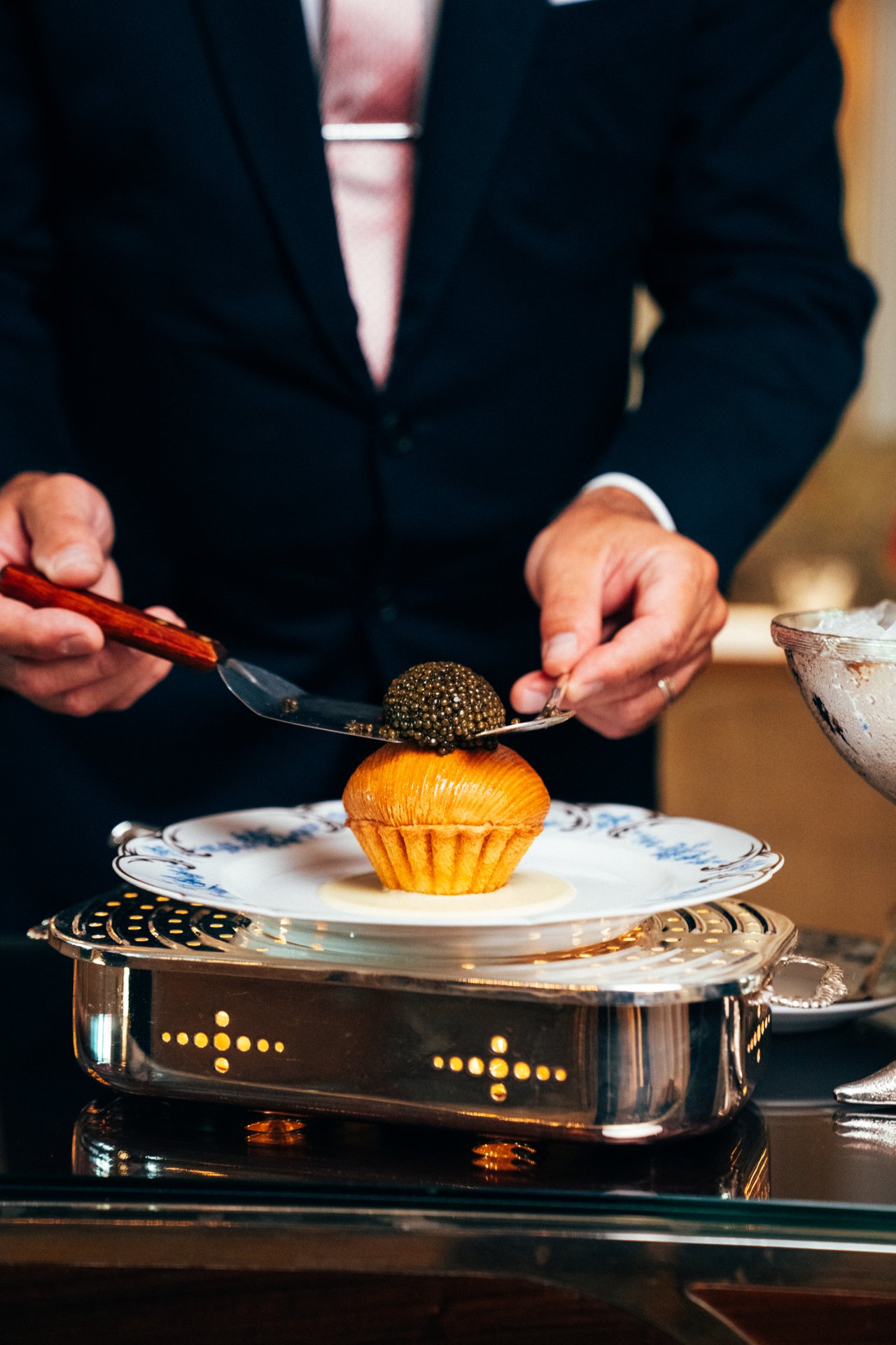 A person slices a dessert topped with black caviar on a dinner plate in a formal setting.