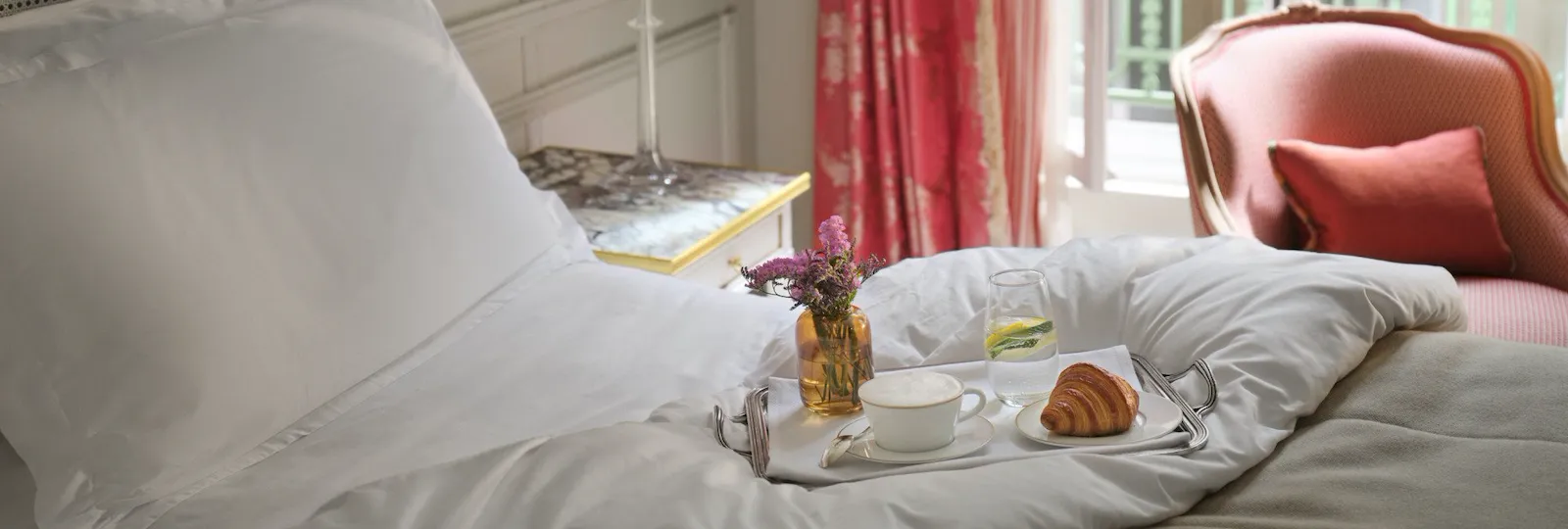 Plan on the top of the bed with a breakfast tray on it, with a cup of coffee, a croissant and a flower arrangement , at Le Meurice, Paris