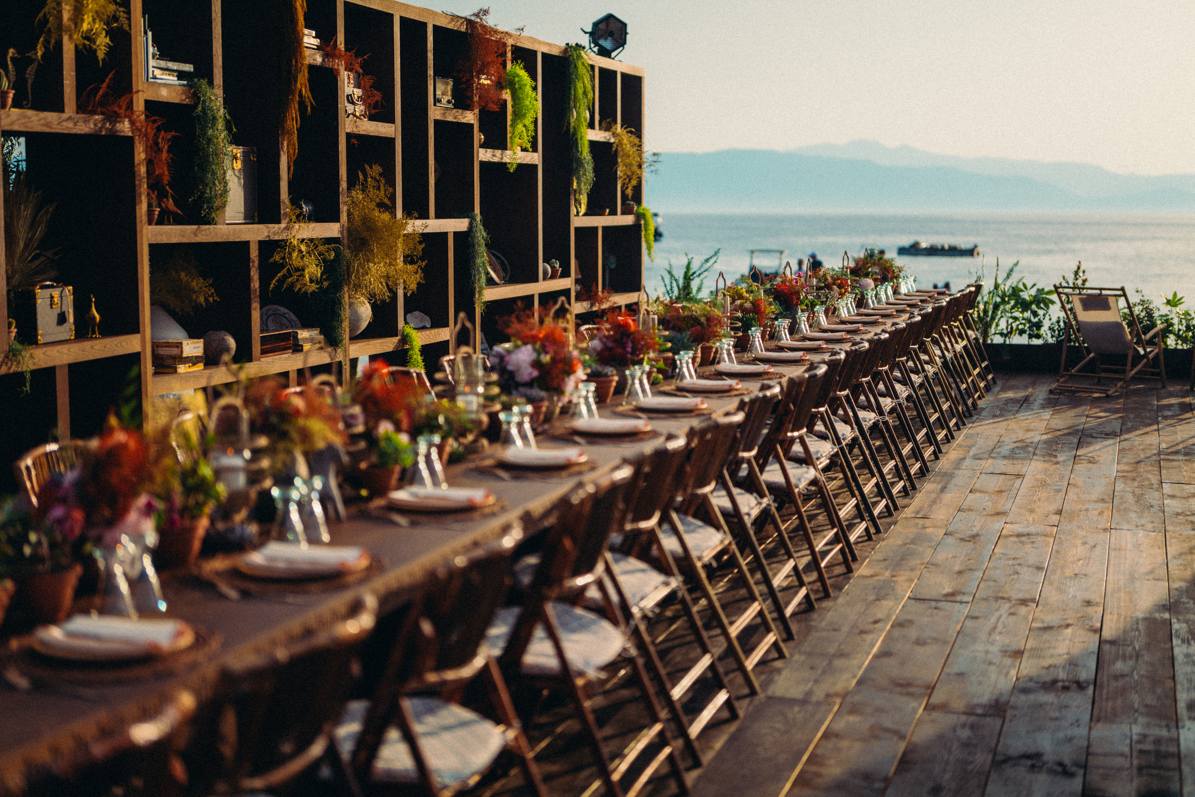 Un bar extérieur rond est agrémenté de hautes chaises en osier et d'une végétation luxuriante aux couleurs orange et verte. Il se trouve sur une terrasse en bois au milieu d'un jardin accueillant et ensoleillé.