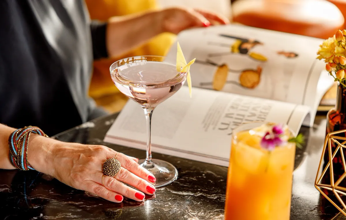 Dettaglio delle mani di una donna che sfogliano una rivista e toccano una coppa con un cocktail a Il Giardino Bar