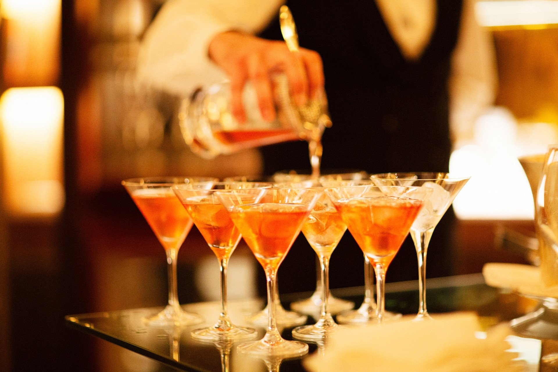 Barman pouring cocktails into several Martini glasses at La Libreria at Hotel Eden, Rome