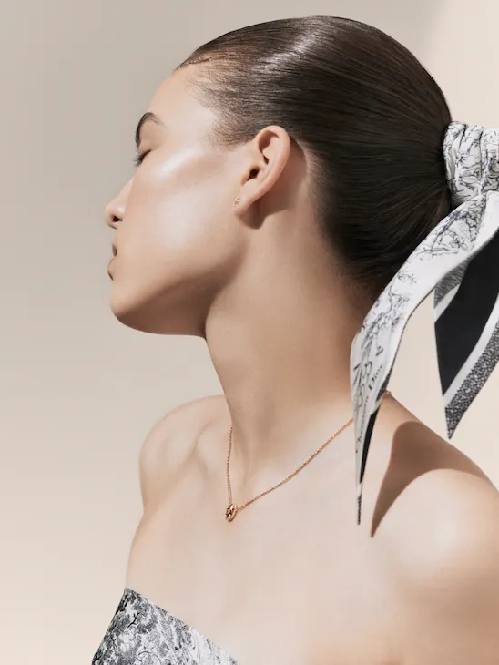 Dior Spa Plaza Athénée's iconography for spa treatments. Here, a light-skin female model posing with her head leaning towards her right side, accessorised with a toile de jouy head band and a short pink gold necklace.