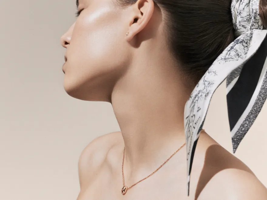 A iconografia do spa Dior Spa Plaza Athénée. Aqui, uma modelo de pele clara coloca a cabeça inclinada para a direita, acessorada com uma faixa de cabeça em tela de jouy e um curto colar em ouro rosa.