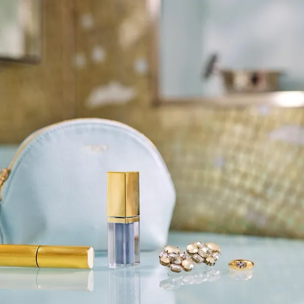 pochette azzurra con rossetto e orecchini oro appoggiati in bagno