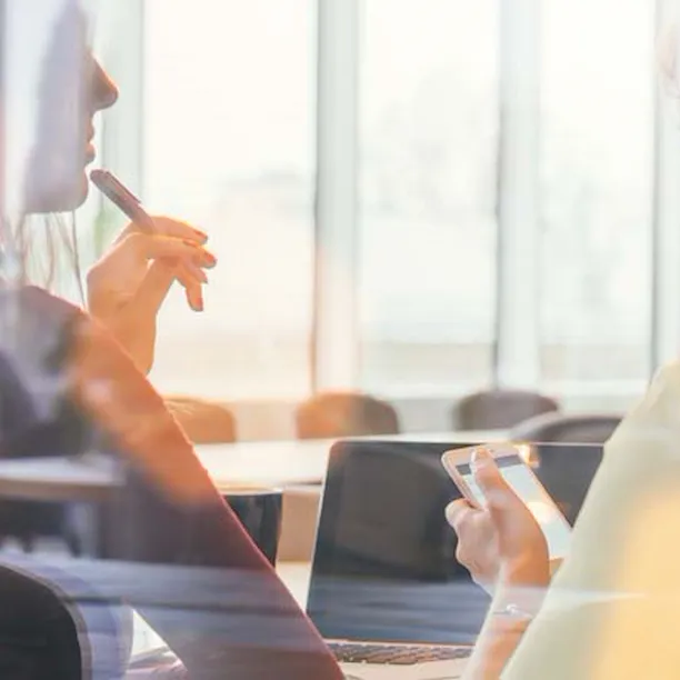 Two woman in meeting room holding mobile phone and a pen