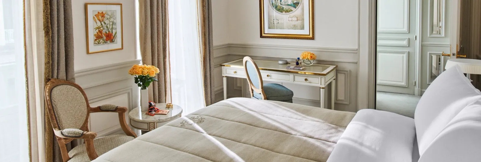 Bedroom in beige and white shades, with queen bed, white wood desk and armchair, at Le Meurice, Paris.