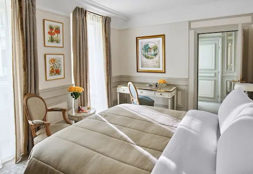 Chambre classique dans les tons blanc et beige, avec lit queen et un un bureau en bois blanc au Meurice, Paris.