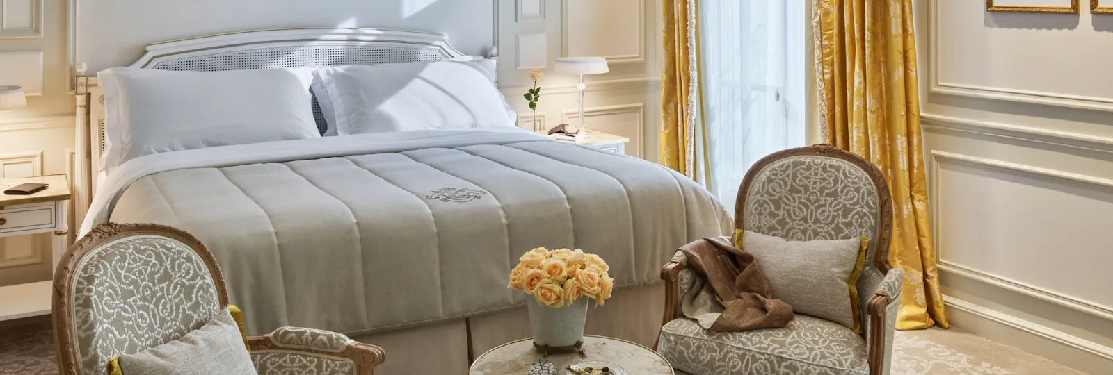 Executive room with beige tones, yellow curtains and yellow roses, two chairs in front of the bed. At Le Meurice, Paris.