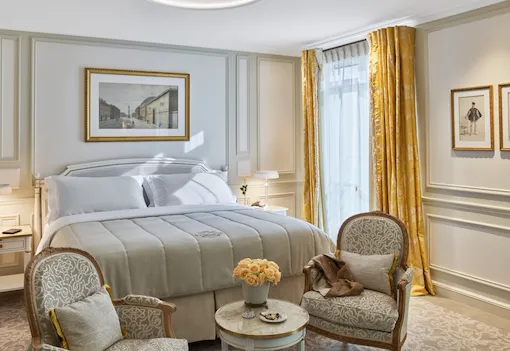 Executive room with beige tones, yellow curtains and yellow roses, two chairs in front of the bed. At Le Meurice, Paris.