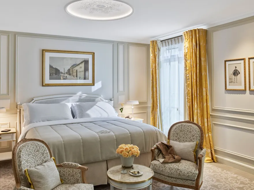Executive room with beige tones, yellow curtains and yellow roses, two chairs in front of the bed. At Le Meurice, Paris.