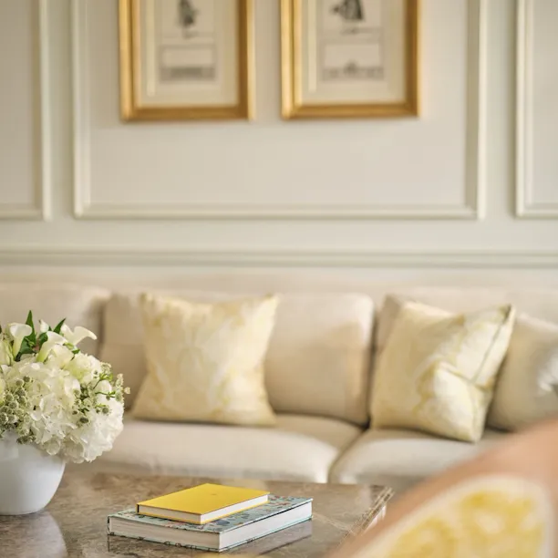 Detail picture of a prestige suite. A marble table with a flower arrangement and two books in visible on the foreground, a sofa in soft beige colours is in the background, at Le Meurice, Paris.