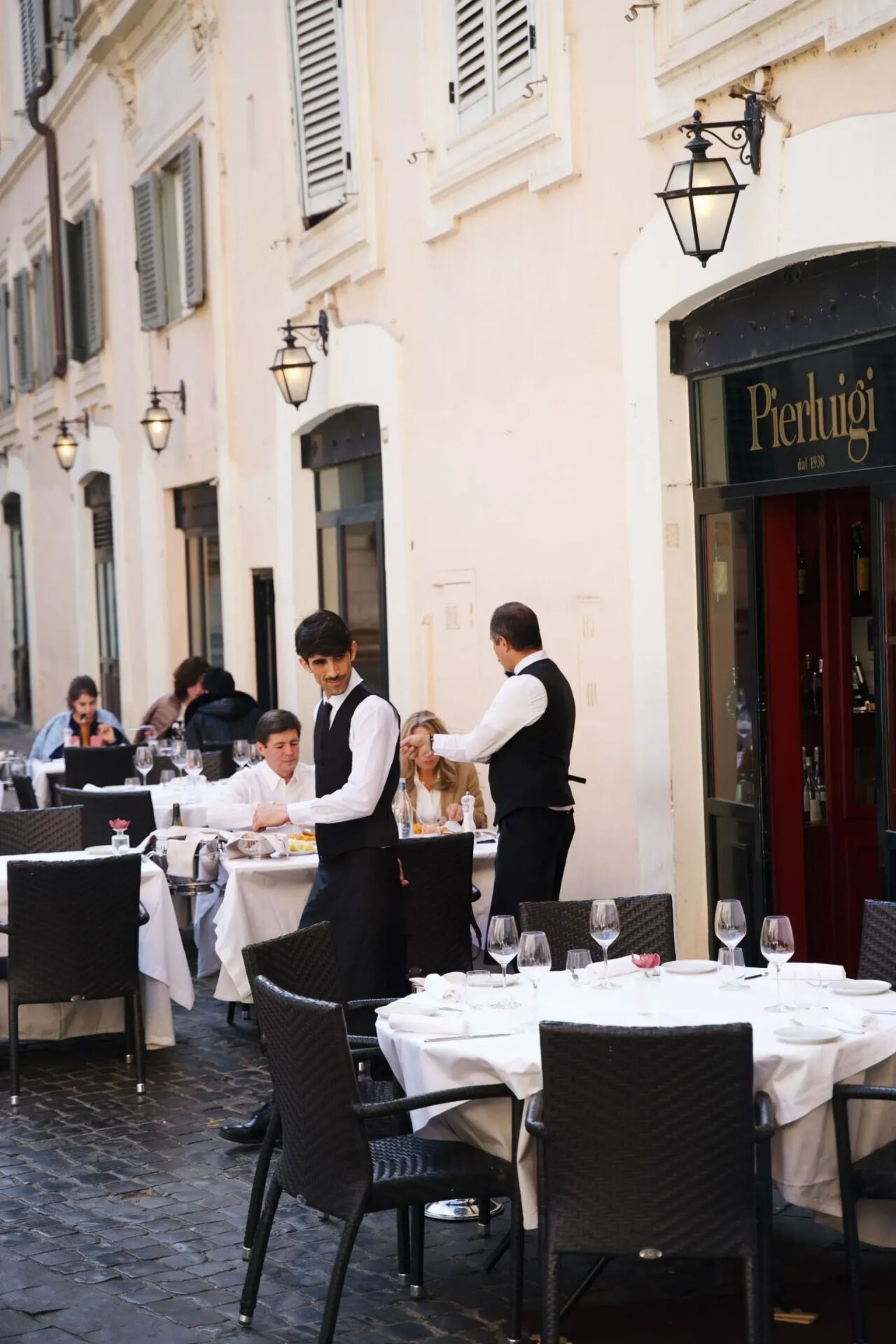 Waiters in front of restaurants among set tables with patrons