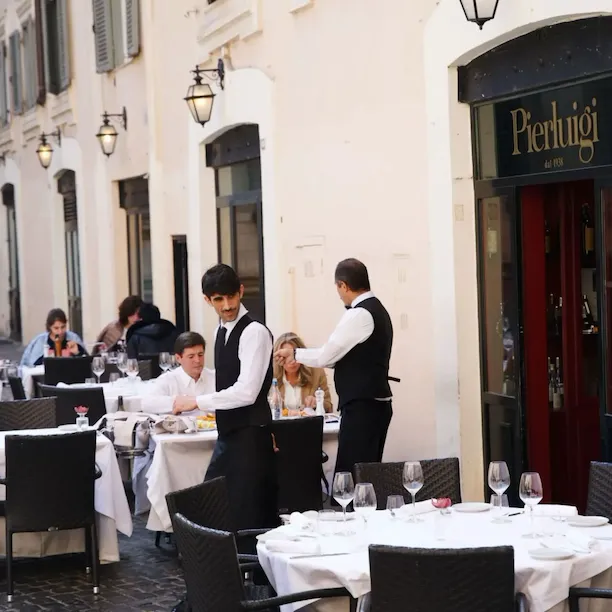 Waiters in front of restaurants among set tables with patrons