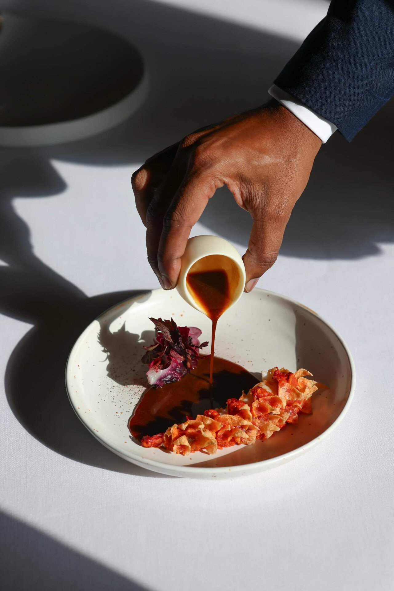It is the picture of a white plate on a white table, containing a sophisticated presentation of crispy blue lobster, celery, bone marrow and lovage, at Le Meurice, Paris. 
