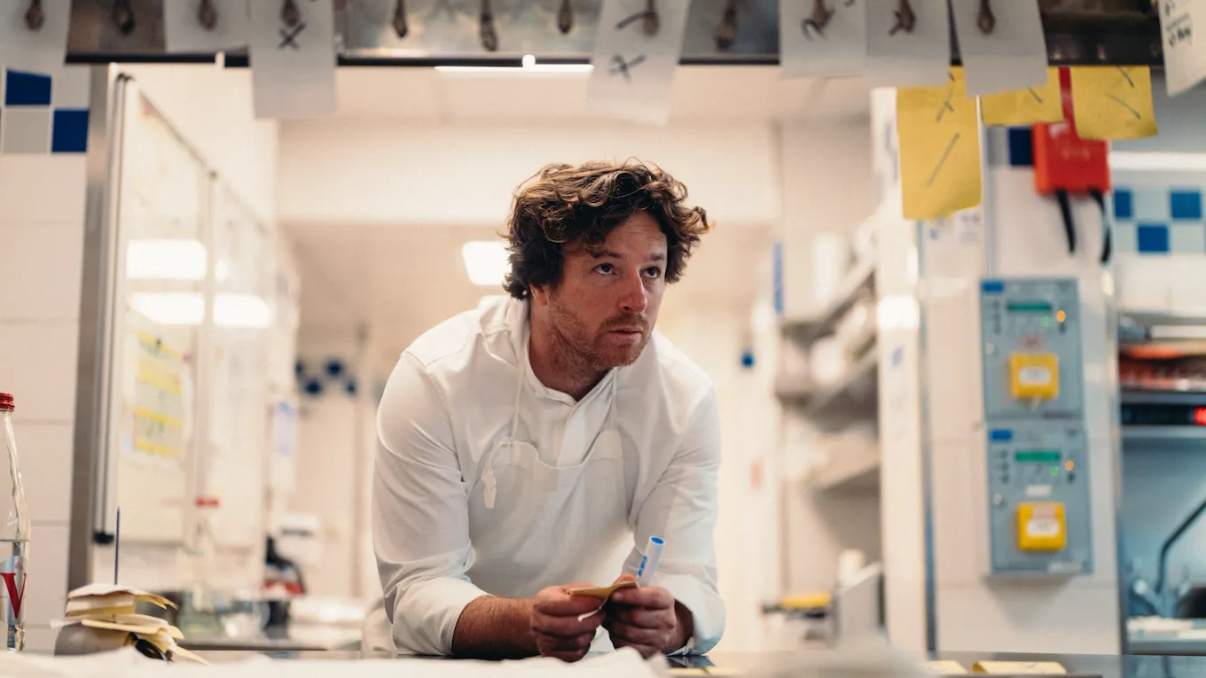 Backstage picture of Chef Jean Imbert leaning on the kitchen counter at Hotel Plaza Athénée, Paris