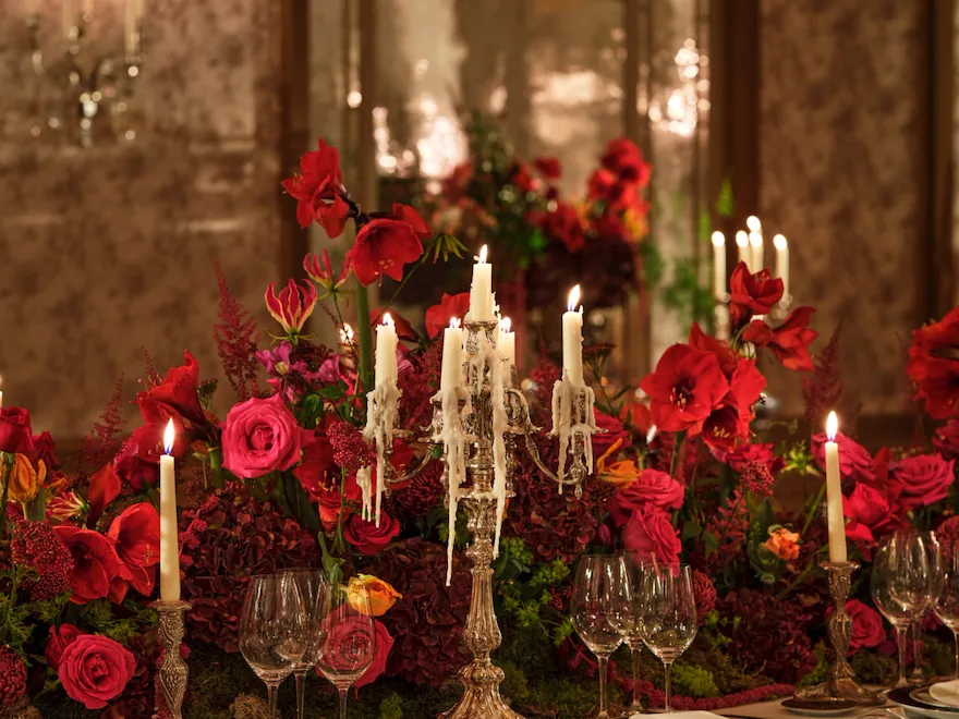 Detail of a dinner set up with red flowers and chandelier captured in Le Salon Haute Couture, at Hôtel Plaza Athénée, Paris - Dorchester Collection.