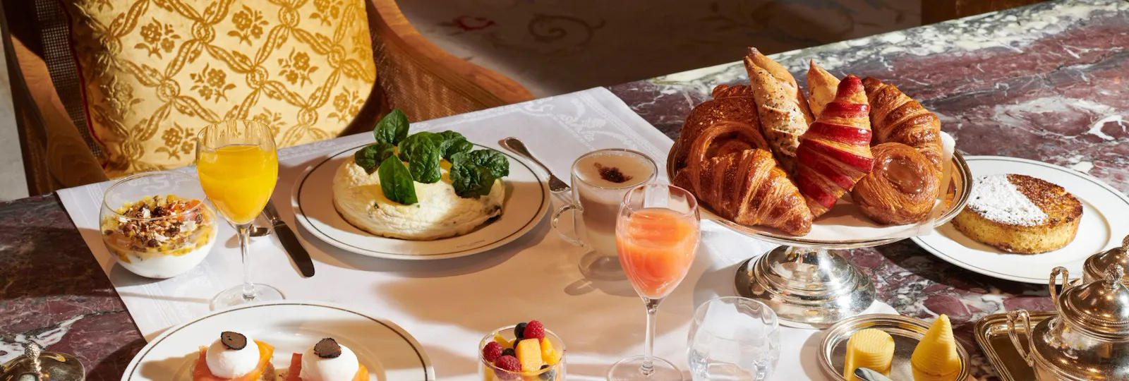 Image d'un brunch au restaurant Jean Imbert au Plaza Athénée. Nous pouvons voir une salade de fruit, des patisseries et vienoiseries, des oeufs, des crêpes, une omelettes et des jus de fruits