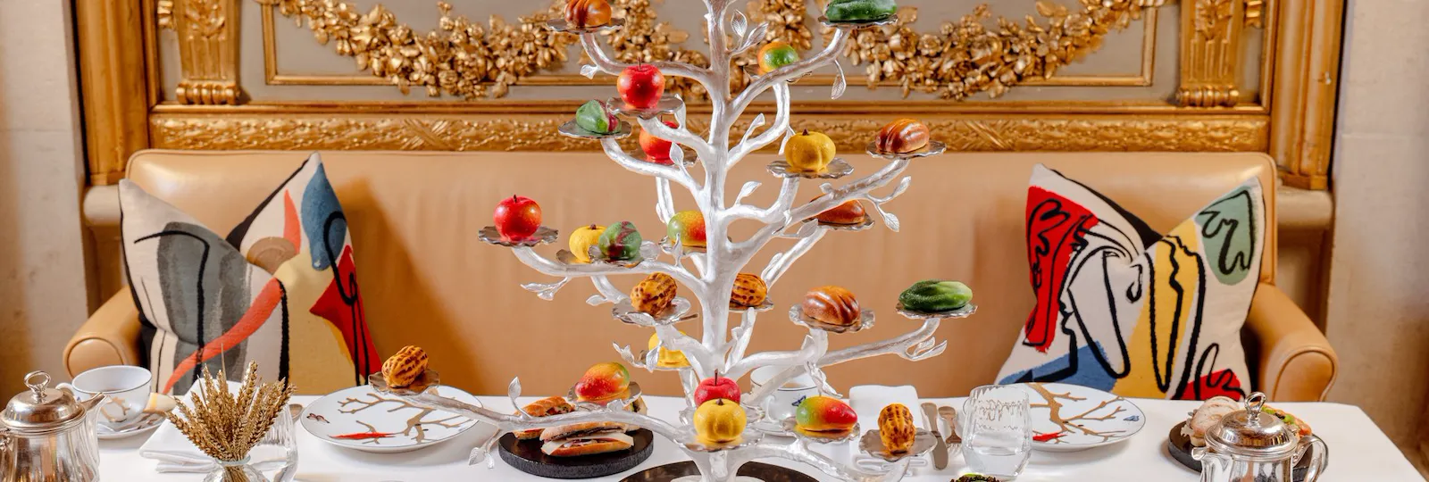 Festive table with a white Christmas tree, plates, glasses, and colorful artwork cushions.