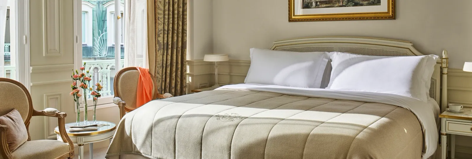 Superior room in beige and white tones with a queen bed and flowers on a low table, at Le Meurice, Paris.