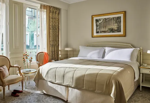 Superior room in beige and white tones with a queen bed and flowers on a low table, at Le Meurice, Paris.