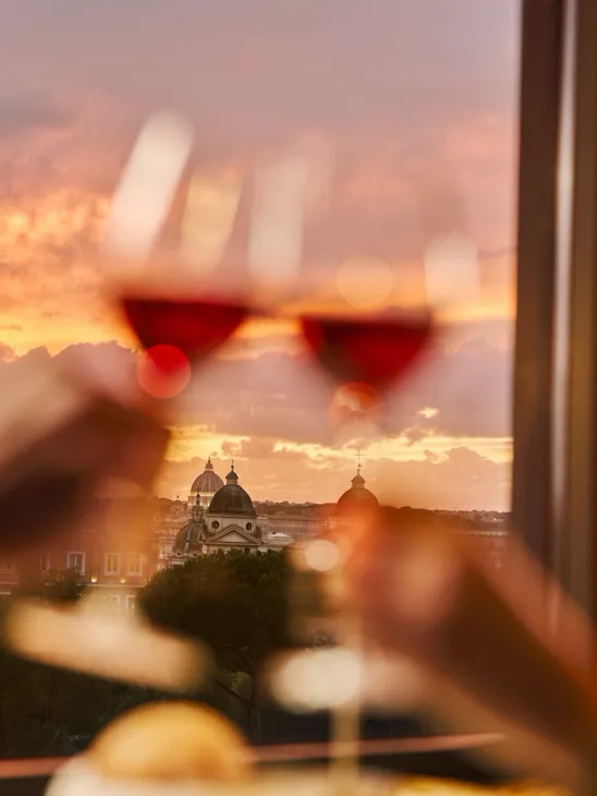 Two glasses of wine clink with a sunset view over a city skyline, creating a romantic mood.