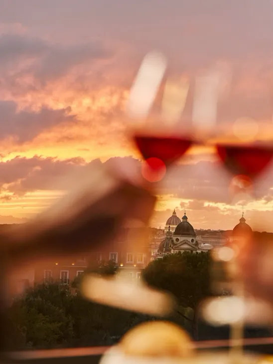 Two glasses of wine clink with a sunset view over a city skyline, creating a romantic mood.
