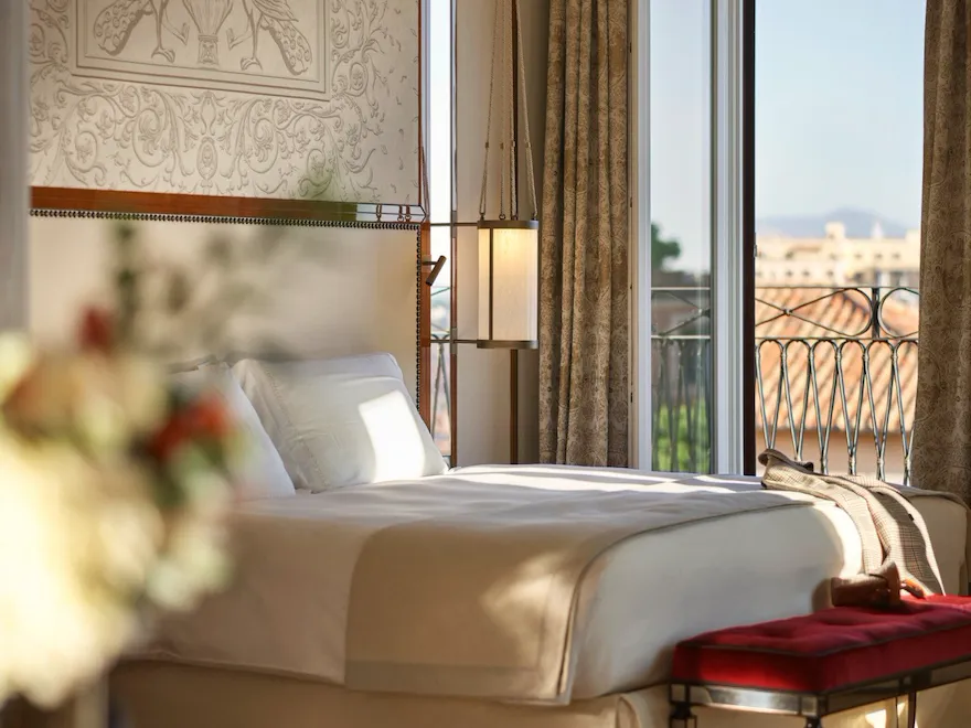 Elegant bedroom Presidential Suite, headboard with peacocks decoration and big window with view of Rome at Hotel Eden