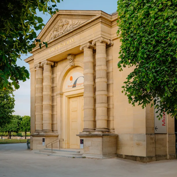 Photo de l’entrée du musée de l’Orangerie avec des arbres autour et un ciel bleu ensoleillé, au musée de l’Orangerie, Paris.