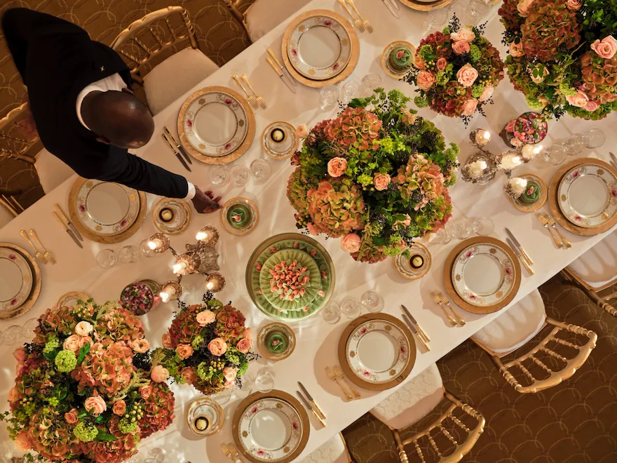 Dinner captured from the top with gold and white tableware, pink and green flowers, green cakes at Le Salon Organza, at Hôtel Plaza Athénée, Paris - Dorchester Collection.