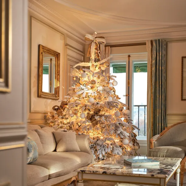 Grande vue sur le salon d’une suite Prestige avec un sapin de Noël décoré, entre le canapé et la fenêtre, au Meurice, Paris