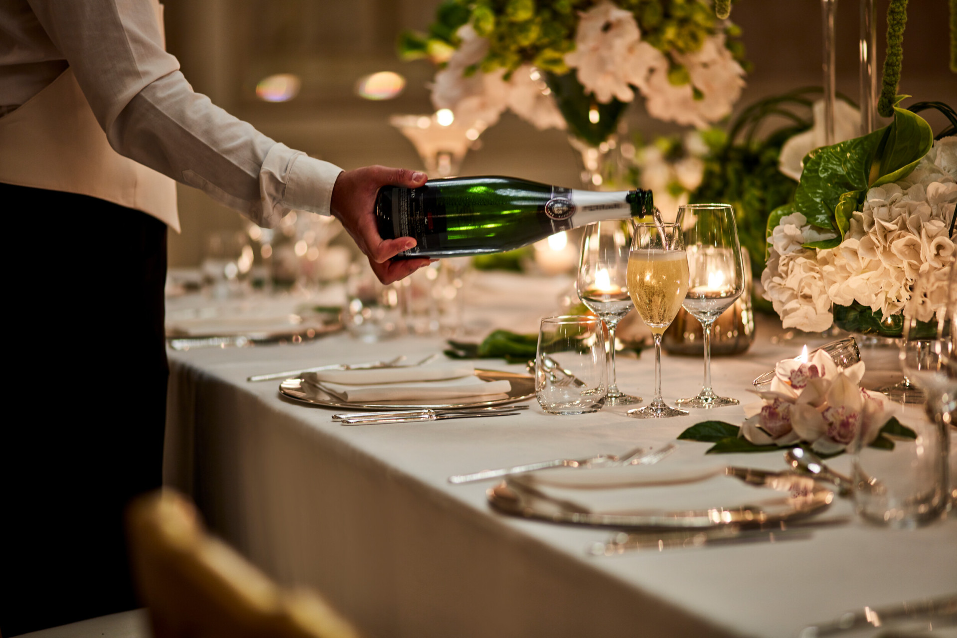 A waiter pouring wine and elegant table set up for a wedding with beautiful fliwer centrepieces