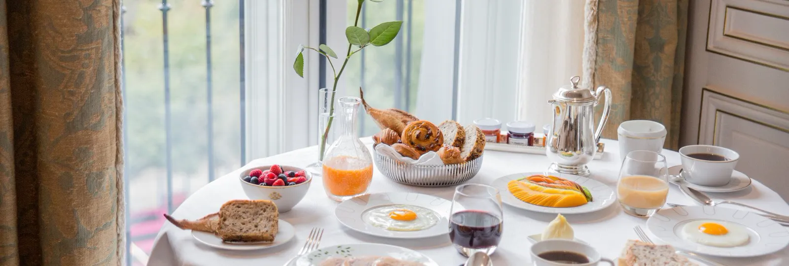 Table de service en chambre avec des plats de petit-déjeuner tels que des œufs, des baies, un panier de fruits et de pâtisseries. Au Meurice, Paris.