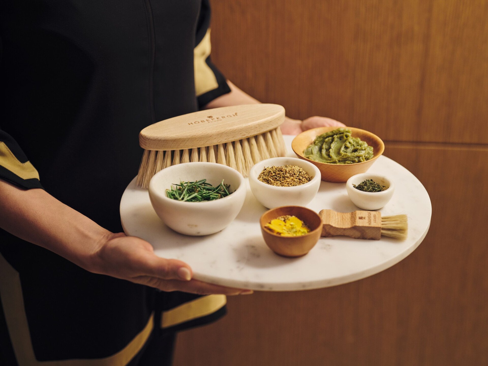 Spa therapist holding tray with brushes, small bowls with alpine herbs