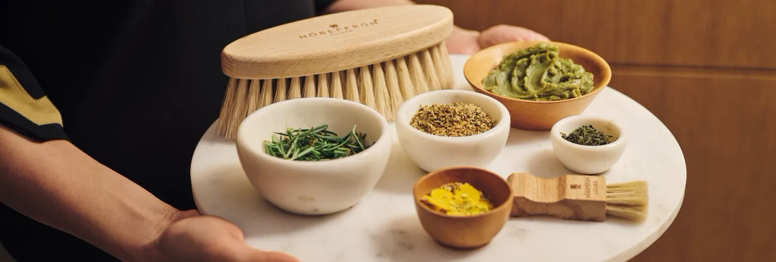 Spa therapist holding tray with brushes, small bowls with alpine herbs