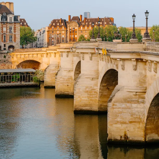 Global view of le Pont Neuf at sunrise with the reflection of the bridge in the water. Orangey buildings in the back of the picture, at Pont Neuf, Paris.