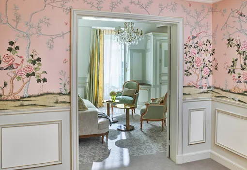Vue lointaine du salon, mettant en valeur le papier peint rose de la chambre, au Meurice, Paris.