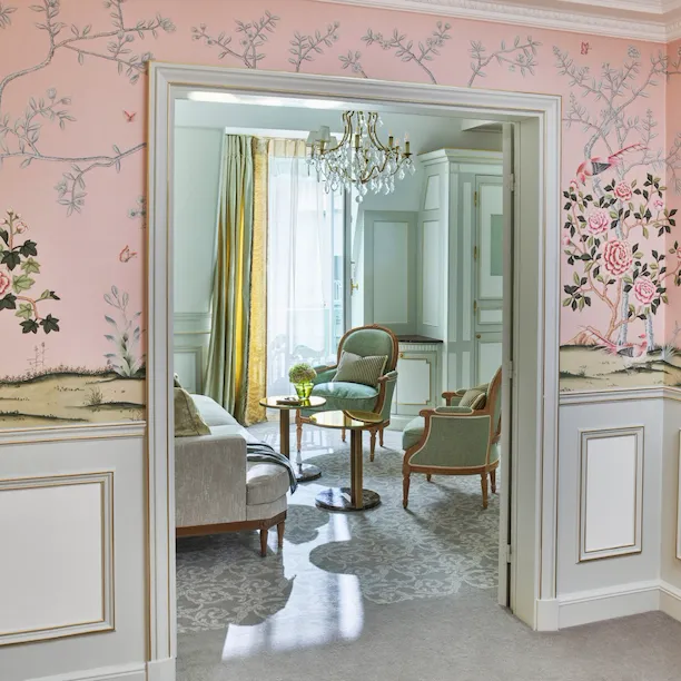 Fotografia ao longe da sala de estar, realçando o papel de parede cor-de-rosa da sala, no Le Meurice, Paris.