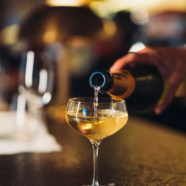Waiter pouring a glass of champaign on the bar counter of Le Relais Plaza, at Hotel Plaza Athénée, Paris